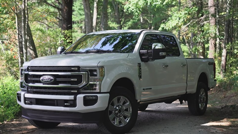 A white Ford Super Duty pickup truck is parked on a dirt road in a forest-like setting