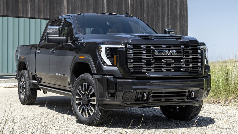 A black 2026 GMC Sierra 2500 HD is parked in front of a modern building on a clear day, surrounded by grasses.