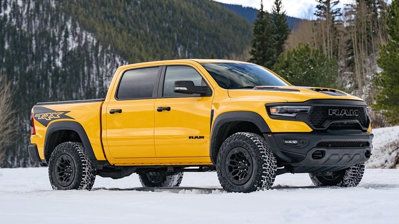 A yellow 2023 Ram 1500 TRX is parked on a snowy landscape with forested mountains in the background.