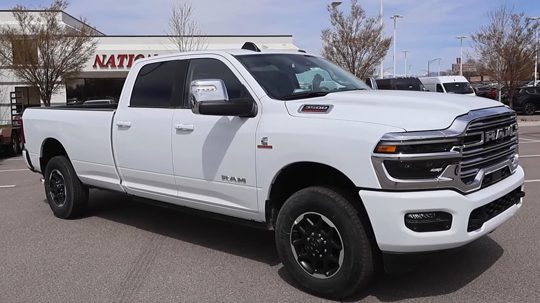 A white Ram 3500 Heavy Duty crew cab pickup truck with a long bed, Cummins Turbo Diesel badging, and a chrome grille parked at a dealership.