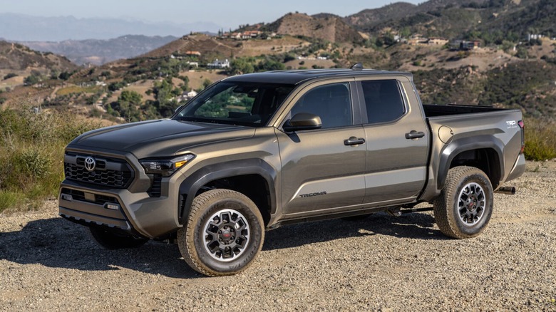 A bronze 2025 Toyota Tacoma parked on a gravel surface with mountains in the background.