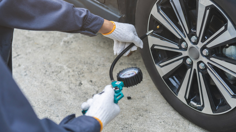 A technician in gloves checking the tire pressure on a passenger car using a handheld gauge