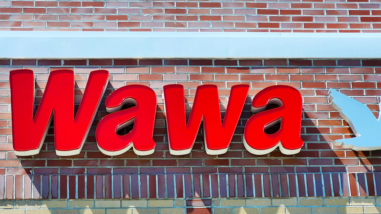 An illuminated WAWA sign on a red brick wall above a storefront