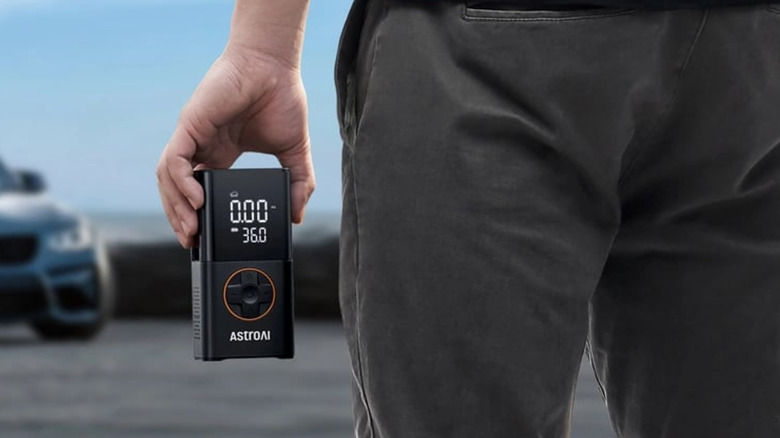 Person holding an AstroAI L7 Tire Inflator in hand, car in the background.