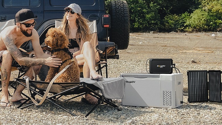 Man and woman sitting outside a car with a BougeRV car fridge on the ground.