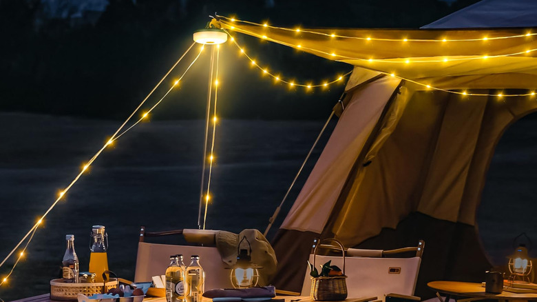 Ogery camping string lights installed around a campsite with tables and chairs set under it.
