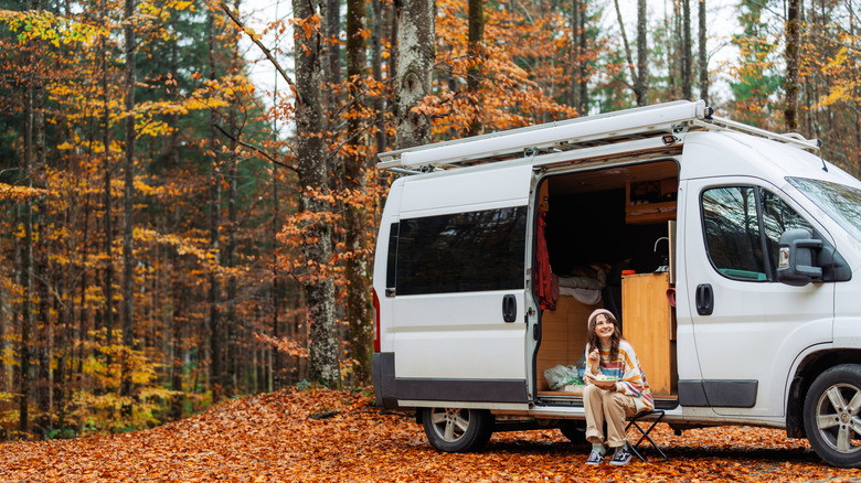 Woman sitting outside a camping van in the fall season.
