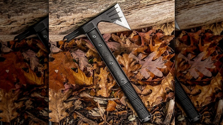 A camping hatchet placed on dead leaves and a wooden piece.