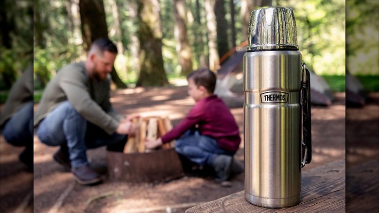 A stainless steel flask placed on wood with a family in the background.