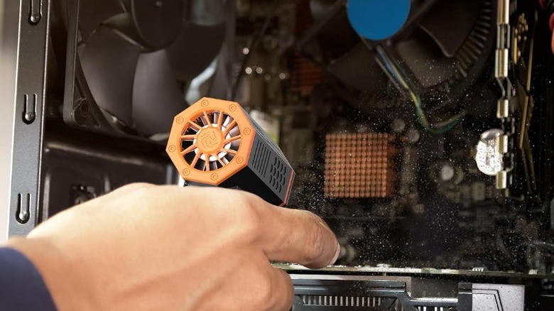 Close-up of hand holding a Wolfbox MegaFlow air duster to clean desktop PC