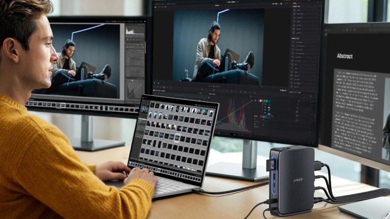 Person sitting at a triple monitor setup with an Anker 13-in-1 docking station on the table