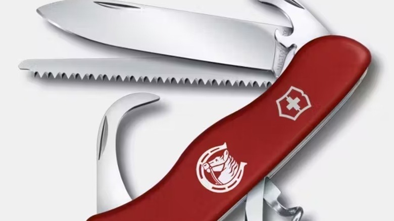 A red Equestrian Swiss Army knife featuring a unique horse-head emblem on the handle, with the hoof cleaner and several other tools extended.