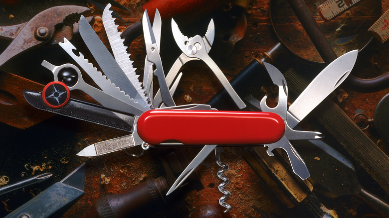 A red Swiss Army knife with multiple tools extended, including scissors, a corkscrew, saw blades, a compass, and screwdrivers.