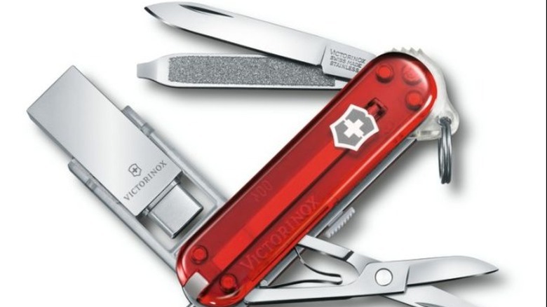 A red translucent Victorinox Swiss Army knife with multiple tools extended, including a USB flash drive.