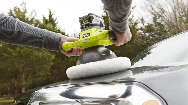A close-up of a person using a Ryobi buffer on a car's hood