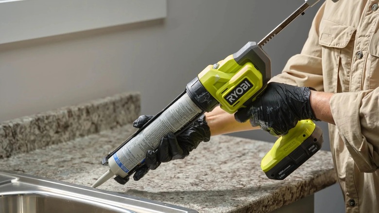 A worker wearing gloves applying caulking around a sink with a Ryobi caulk gun
