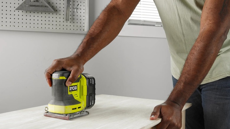 A person sanding a tabletop with a Ryobi sheet sander