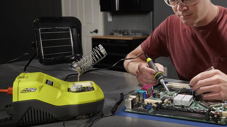 A person wearing safety glasses working on a computer motherboard with a Ryobi soldering station