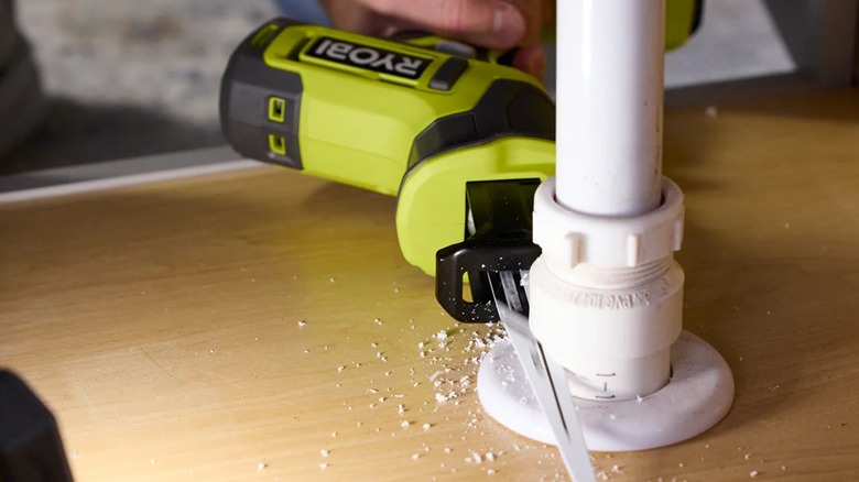 A person cutting a PVC pipe with a Ryobi reciprocating saw