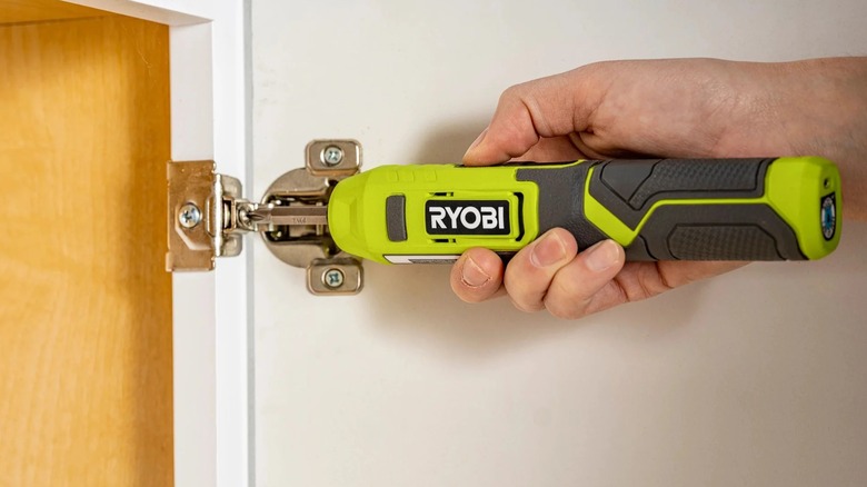 A close-up of a person fixing a door hinge with a Ryobi screwdriver