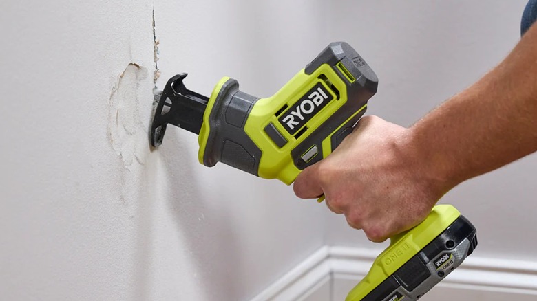 A person cutting into a wall with a Ryobi reciprocating saw