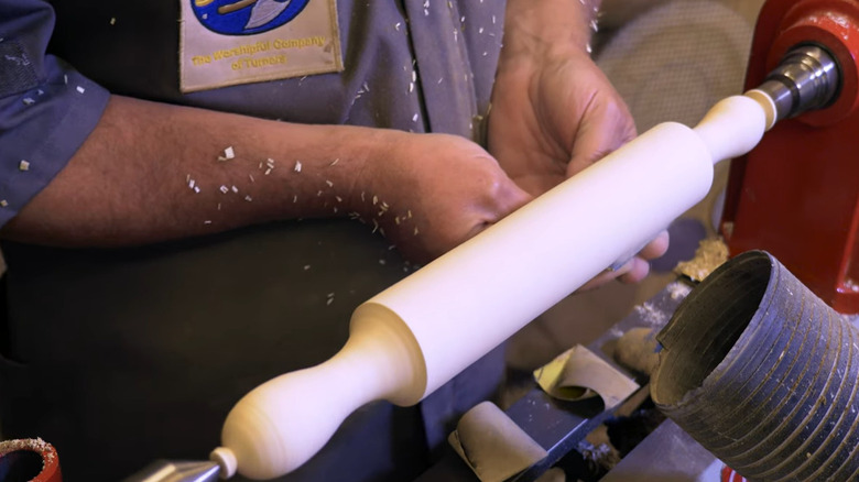 A person makes a rolling pin on a wood lathe.