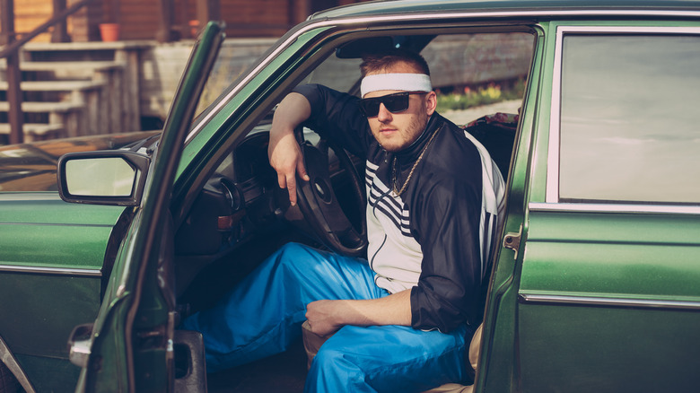 Man wearing sunglasses sitting in a green car with the driver's side door open