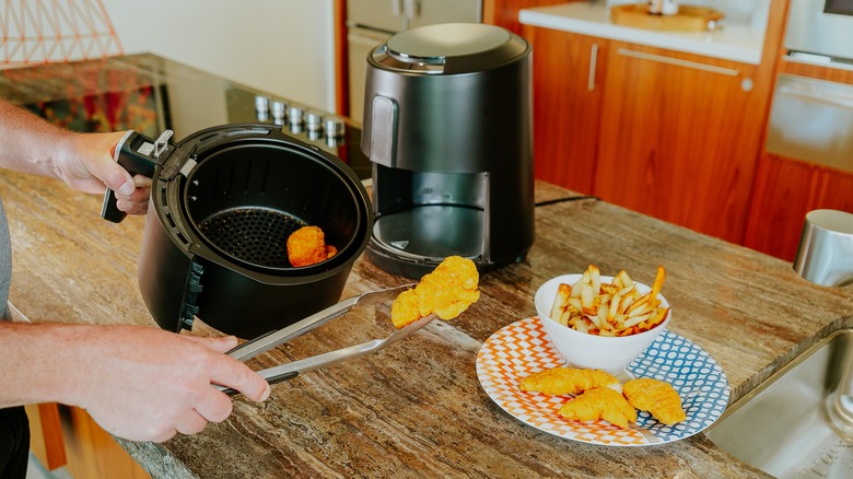 man taking chicken out of small air fryer