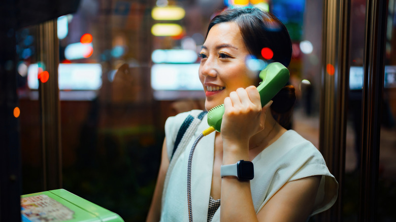 A young Asian woman using public telephone booth at night.