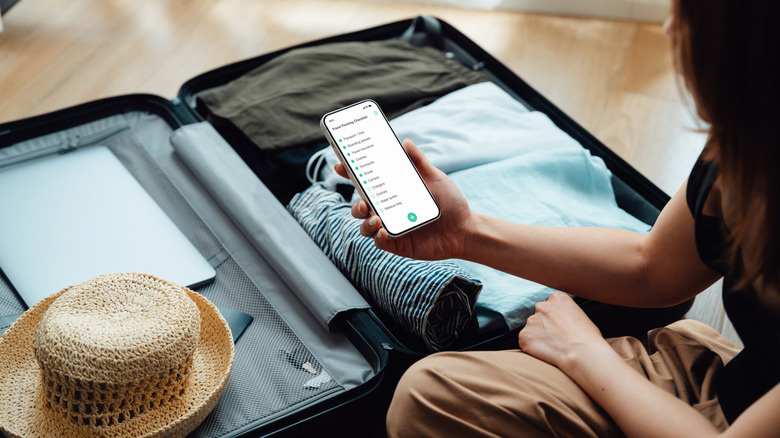 A woman using a smartphone while she packs for a trip.
