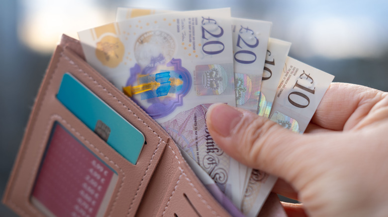 Hand pulls GBP currency from a wallet