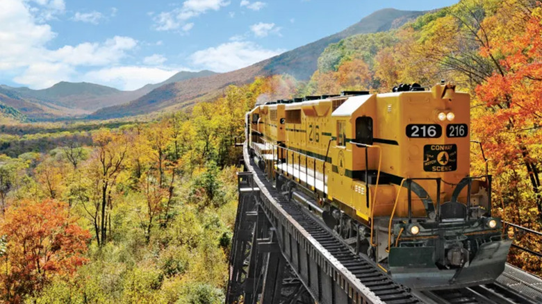A yellow train riding around an autumn landscape