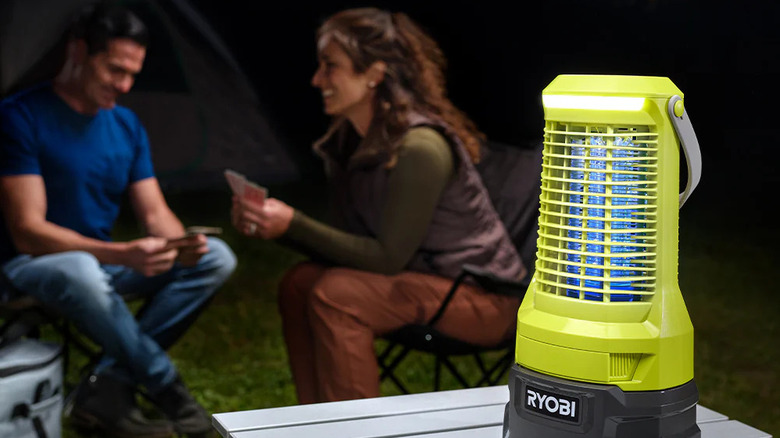 A neon green Ryobi 18V ONE+ Bug Zapper on a table, with a couple sitting in chairs next to their tent in the background.
