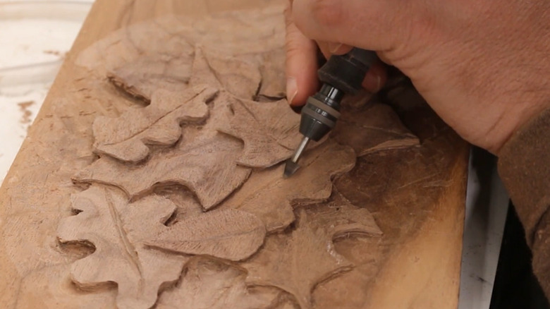 A person carving intricate designs into a plank of wood
