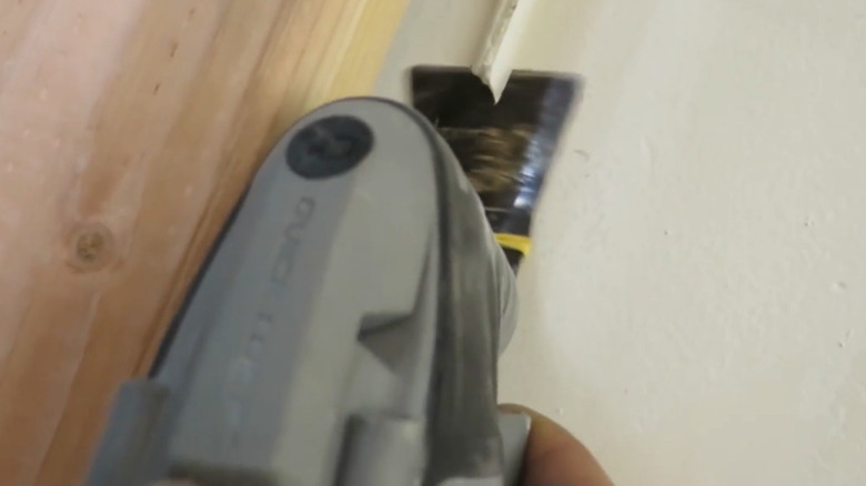 A Dremel rotary tool cutting away caulk from a window frame