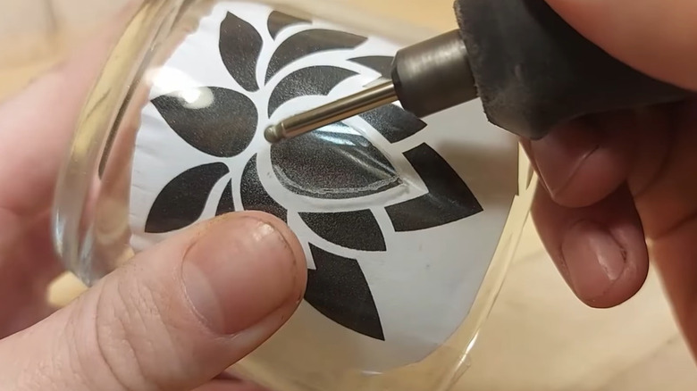 A person engraving a glass cup with a rotary tool