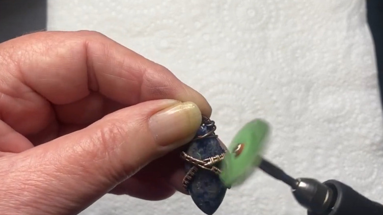 A person polishing a necklace with a rotary tool