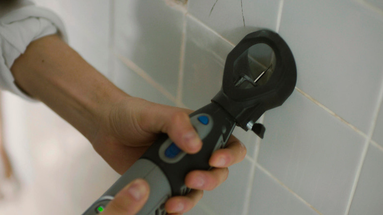 A person removing grout from their bathroom wall tiles
