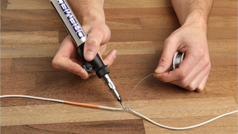 A person soldering a faulty electrical wire