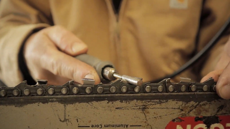 A person using a rotary tool to sharpen a chainsaw