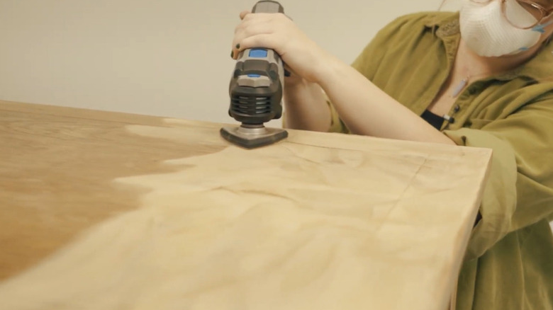 A person wearing a face mask and sanding a coffee table