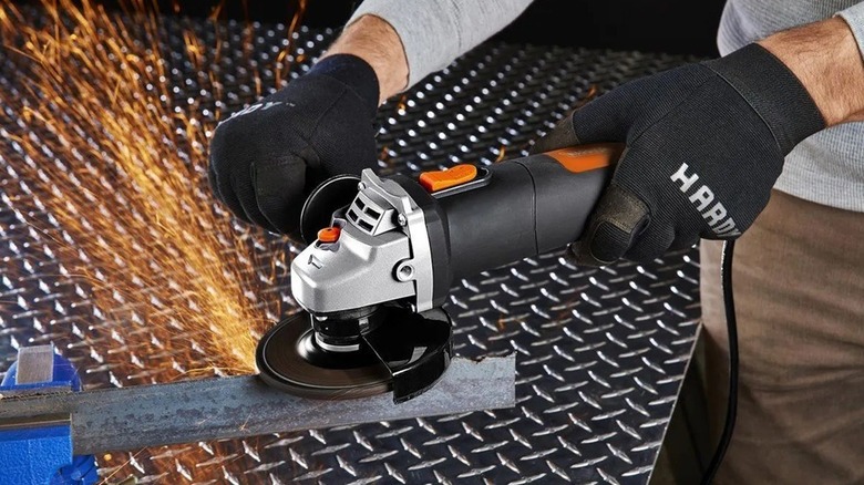 Person wearing safety gloves using angle grinder on a piece of metal held in a vise