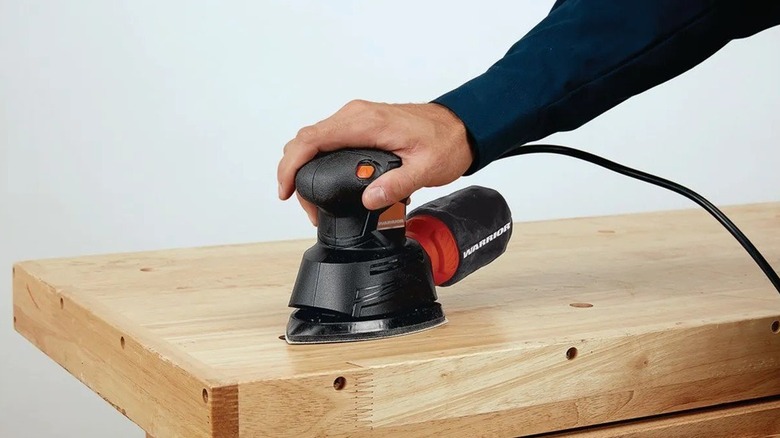 A person using detail sander on a wooden tabletop