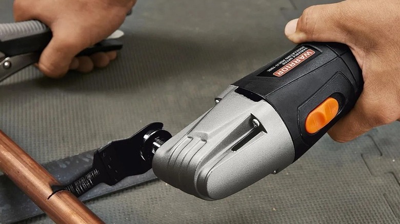 Person using oscillating multi-tool to cut a length of copper pipe