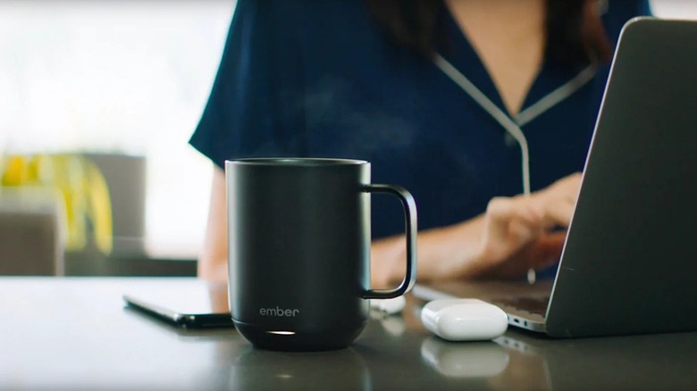 An Ember heated cup, person working on laptop in background.