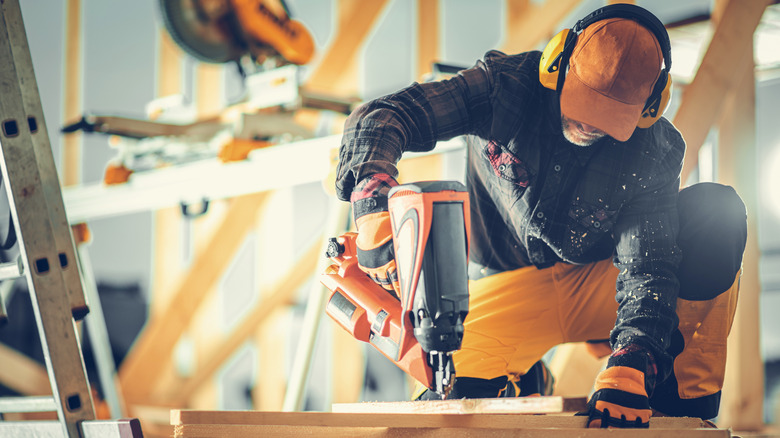 DIYer using nailer with miter saw in background