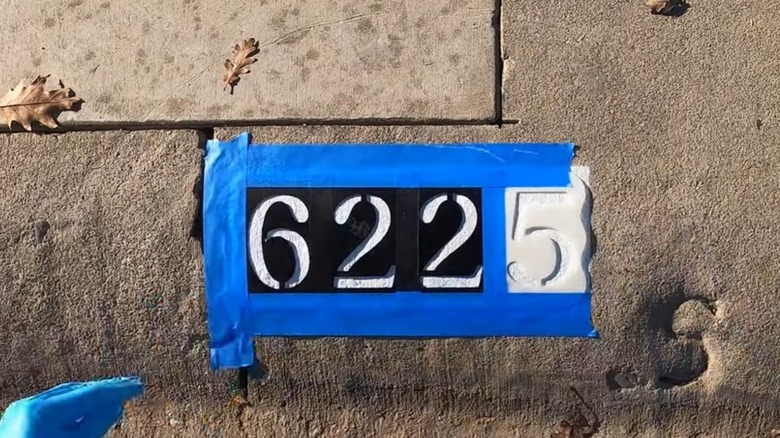 Person painting numbers on curb
