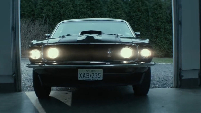 The front view of John Wick's 1969 Silver Mustang Mach 1, with the quad headlights turned on.