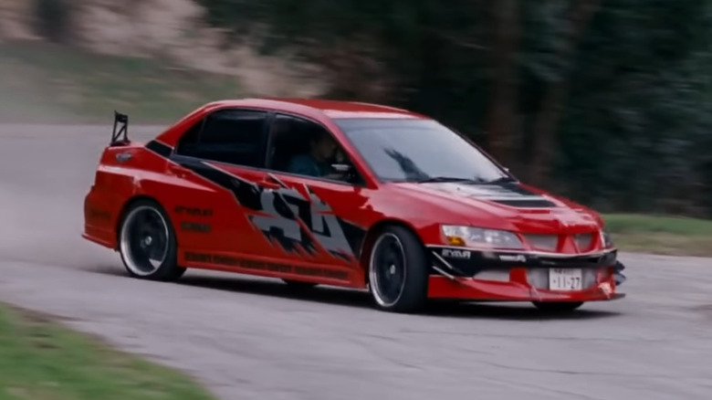 A red Mitsubishi Evo IX drifting around a winding mountain road, left-three quarter view visible.