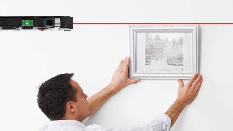 A person installing a painting using the Aiktryee laser leveling tool
